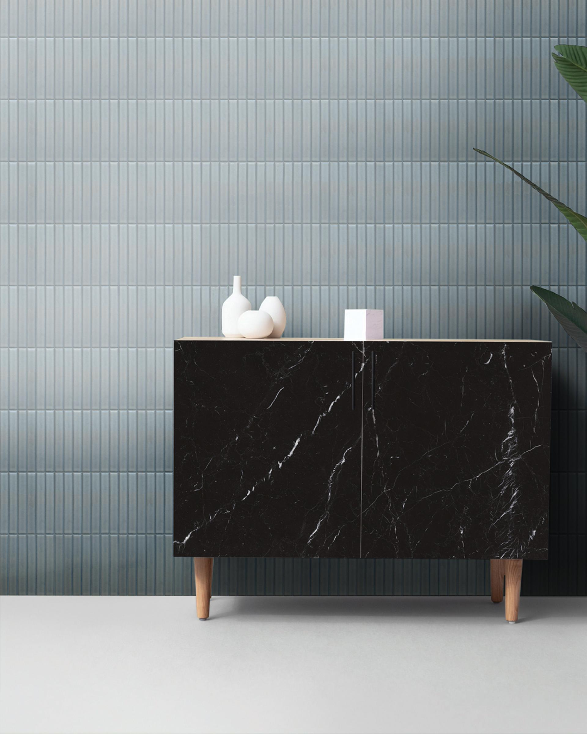 Porcelain mosaic tiles in soft blue tones on a wall, complemented by a sleek black cabinet and decorative vases.