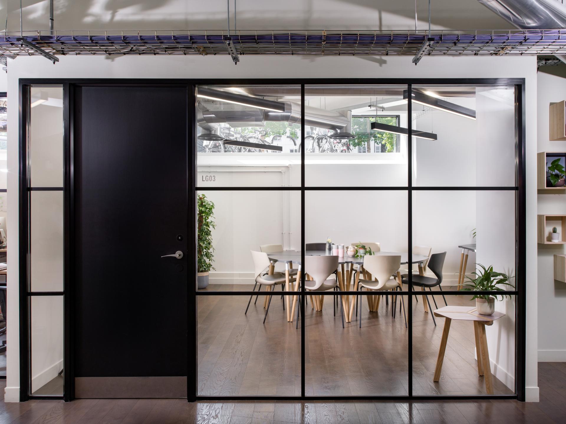 Contemporary office meeting room with glass walls, showcasing a round table and modern seating, emphasizing flexible workplace design.