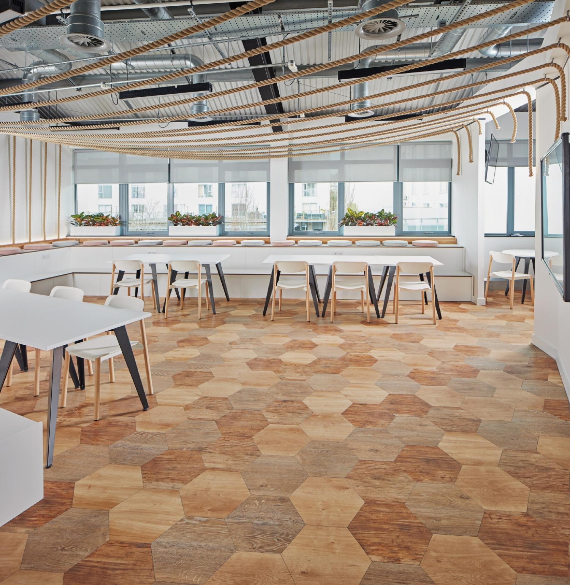Modern office interior featuring hexagon-patterned wood flooring, natural lighting, and minimalist furniture design.