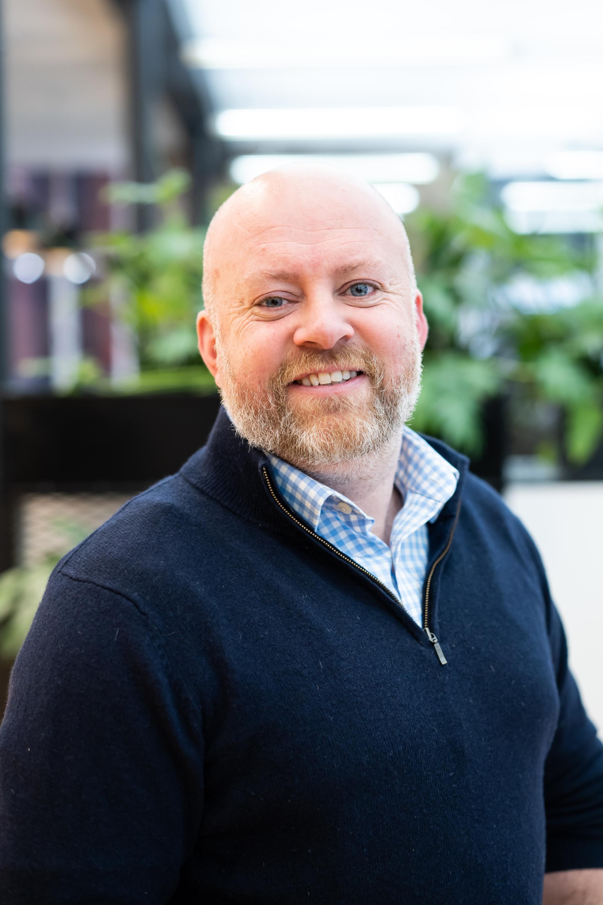 Professional man smiling in an urban green space, highlighting the built environment's role in addressing climate sustainability.