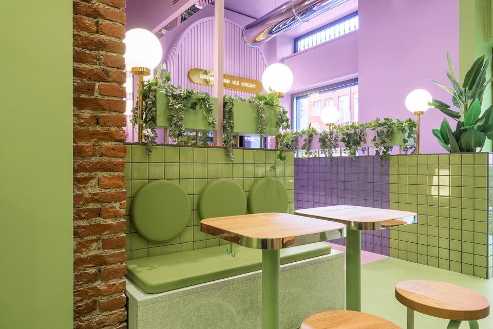 Bright candy-colored interior design featuring green seating, playful decor, and plants at Bun burger restaurant in Milan.