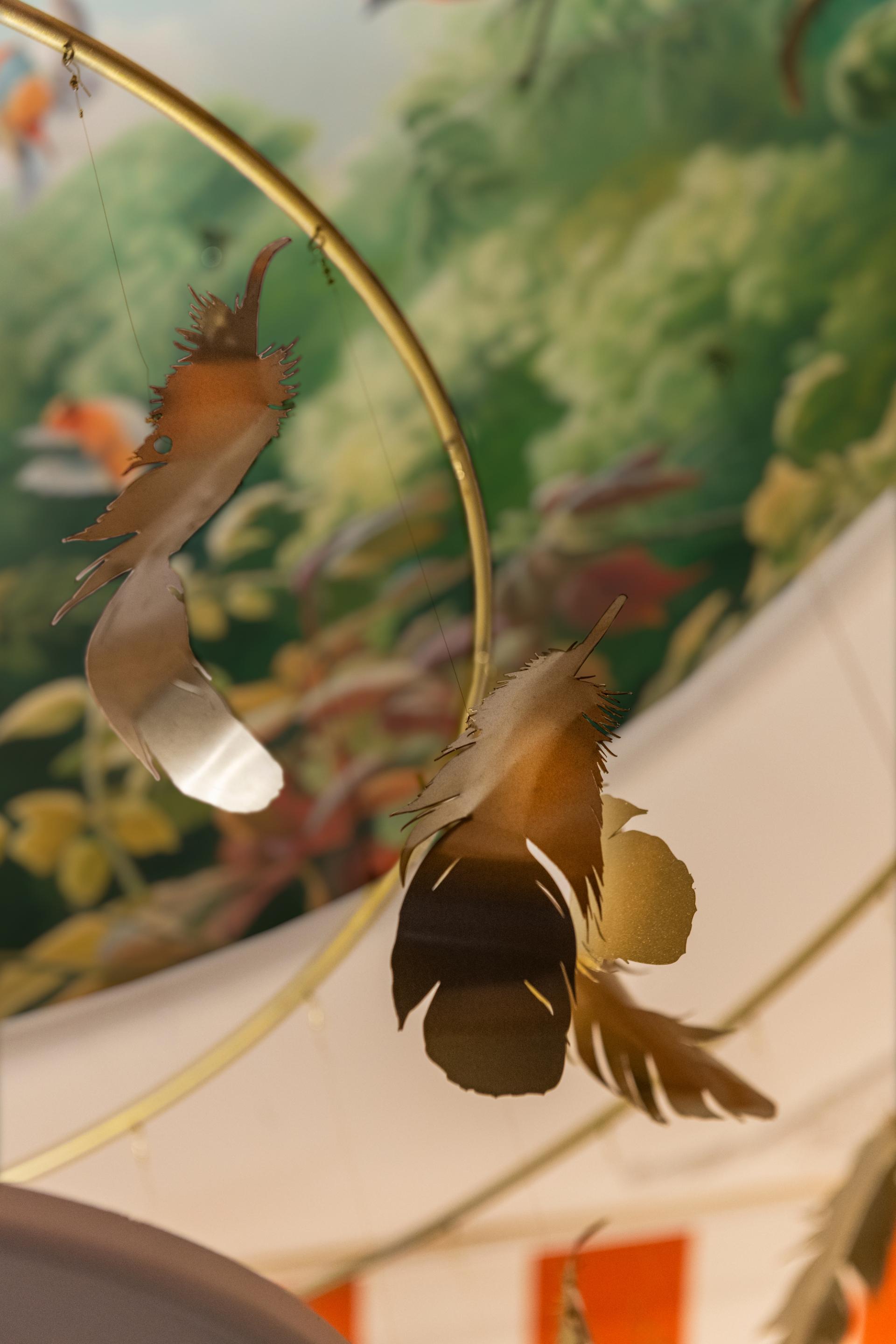 Delicate paper cutouts resembling leaves hang from a circular frame below a vibrant mural in Brixton's bar design.