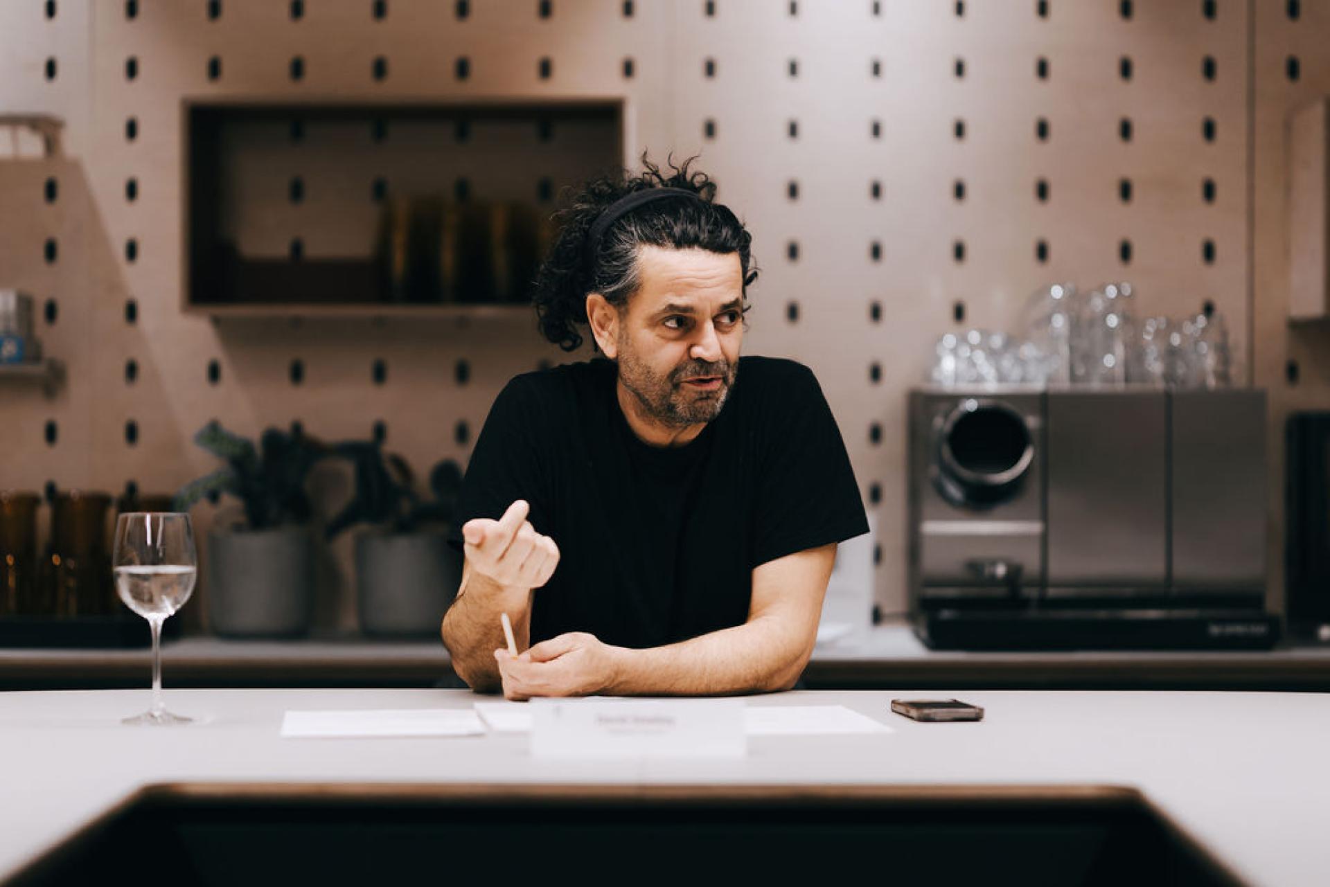 A man gestures during a discussion about sustainable biomaterials at a modern kitchen table setting.