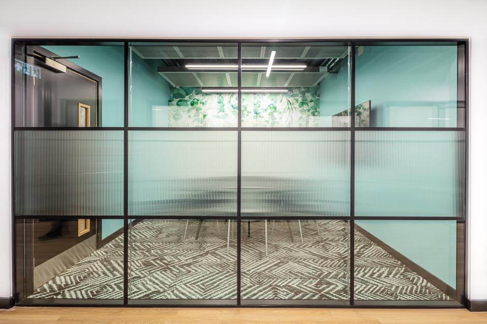 Modern glass meeting room with vibrant decor and stylish flooring, showcasing a flexible workspace environment at The Bee House.