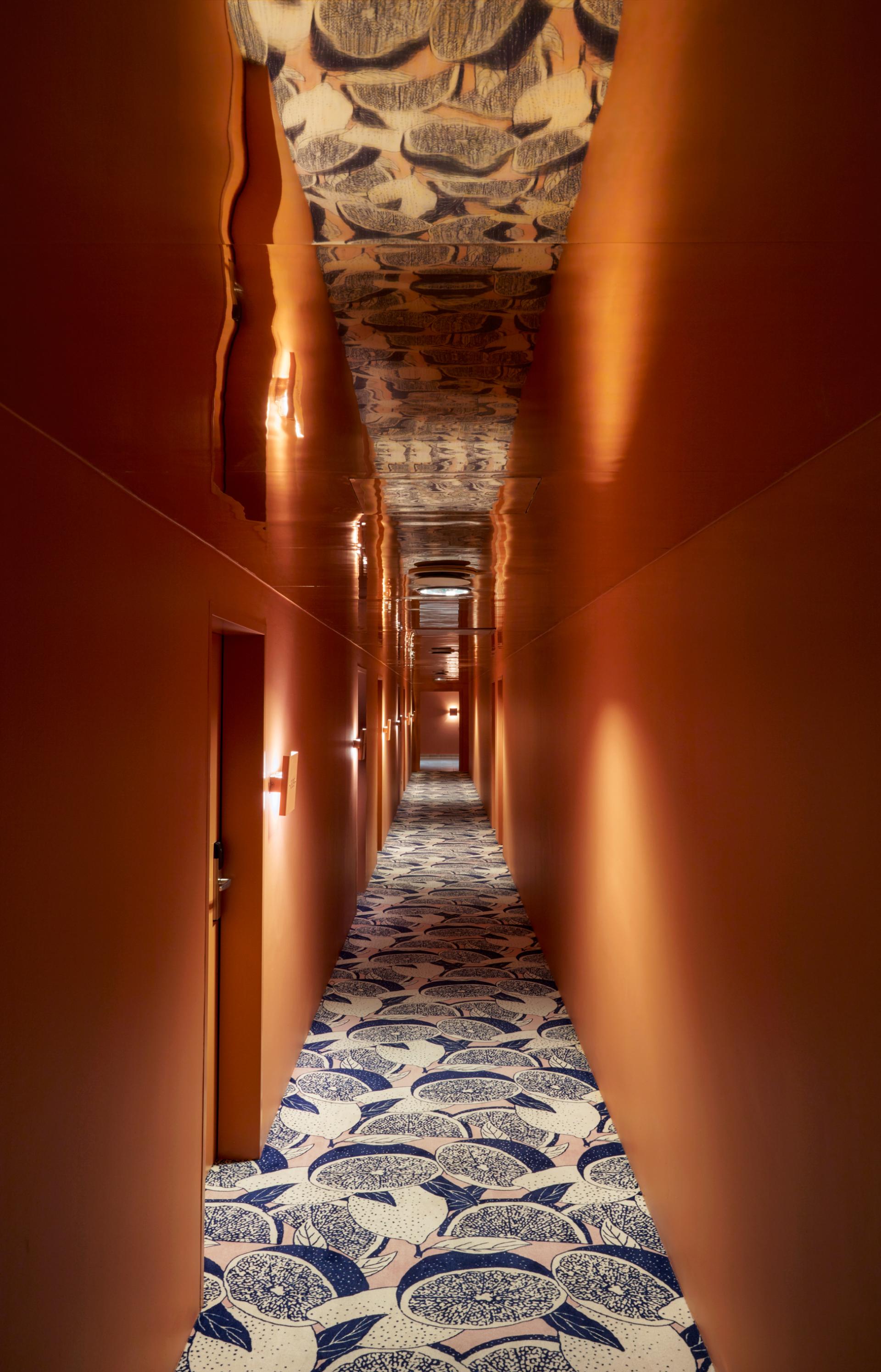 Long hallway at Max Brown Hotel in Vienna, featuring warm orange walls and artistic floral carpet design.