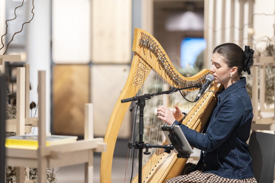 A musician playing the harp and singing at Material Source Studio's third anniversary celebration in Manchester.