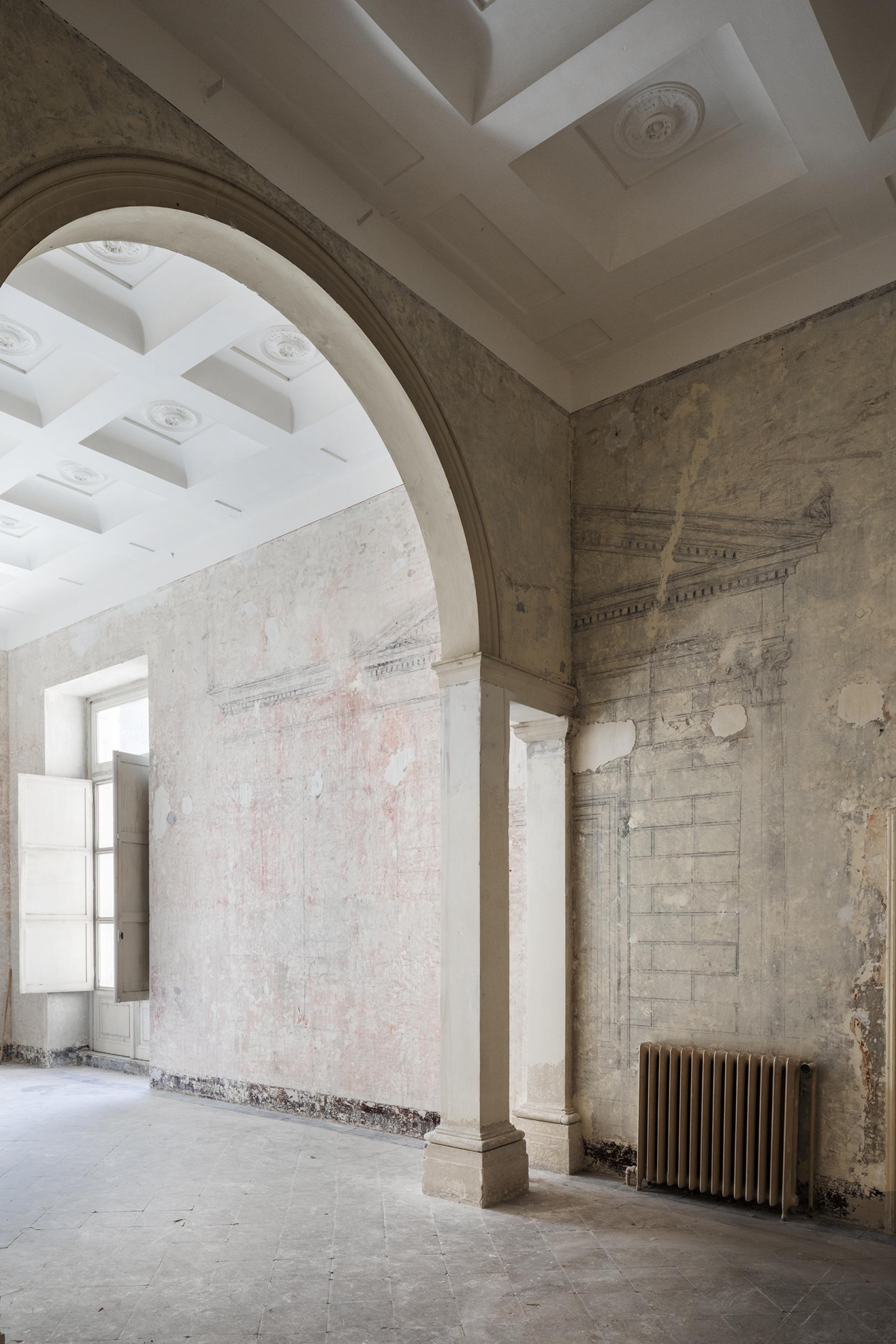 Spacious interior of Palazzo Brancaccio featuring textured walls, arched doorway, and natural light from open windows.