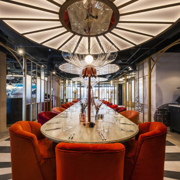Luxurious dining space featuring plush orange chairs and an artistic chandelier, embodying a whimsical Wonderland theme.