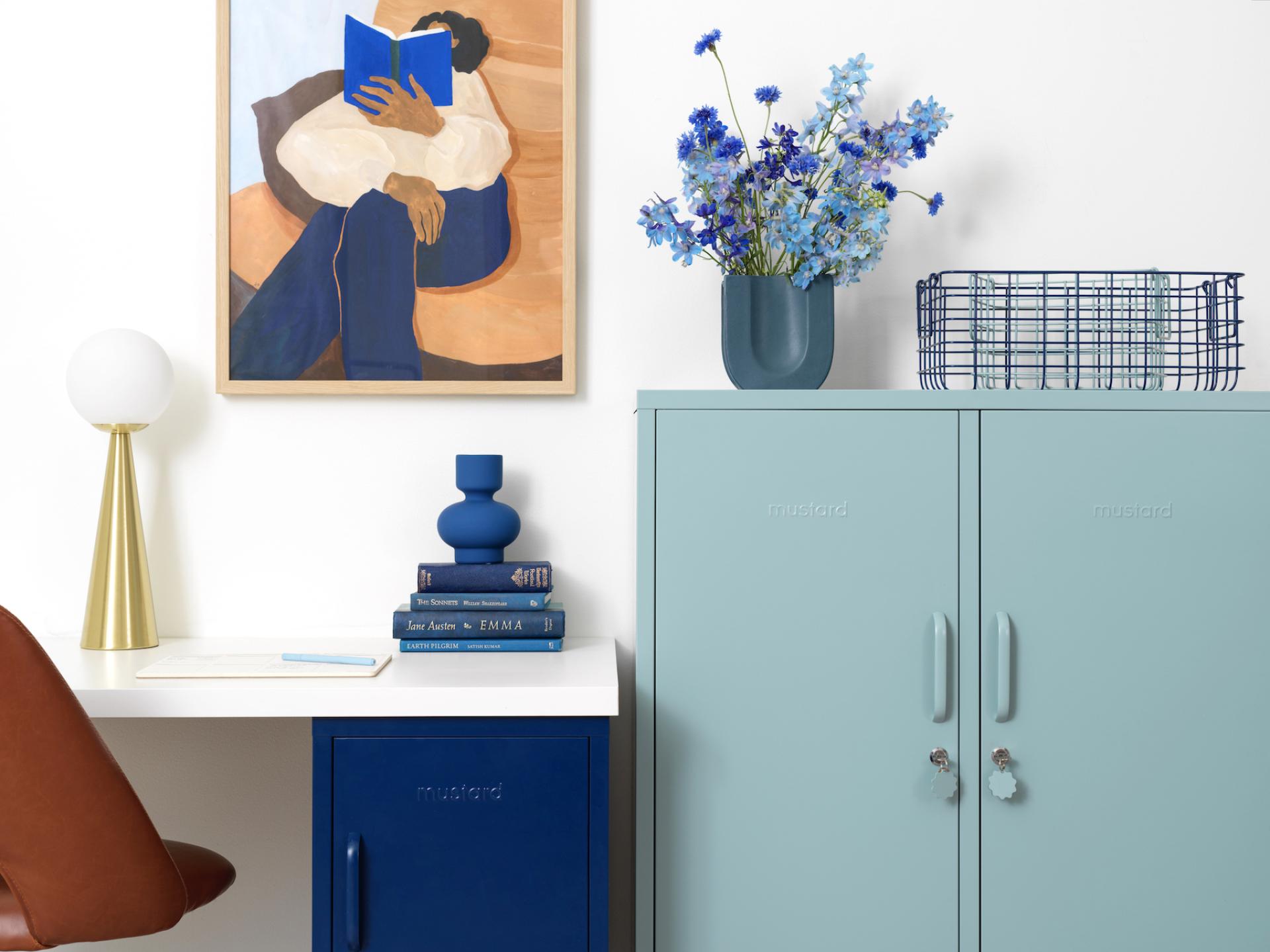 A vibrant home office featuring Mustard Made furniture, colorful decor, a floral arrangement, and an artistic wall painting.