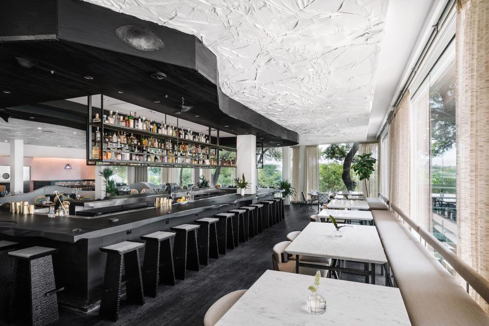Modern bar with a black countertop, shelves of spirits, and minimalist decor in a mid-century hotel in Austin.