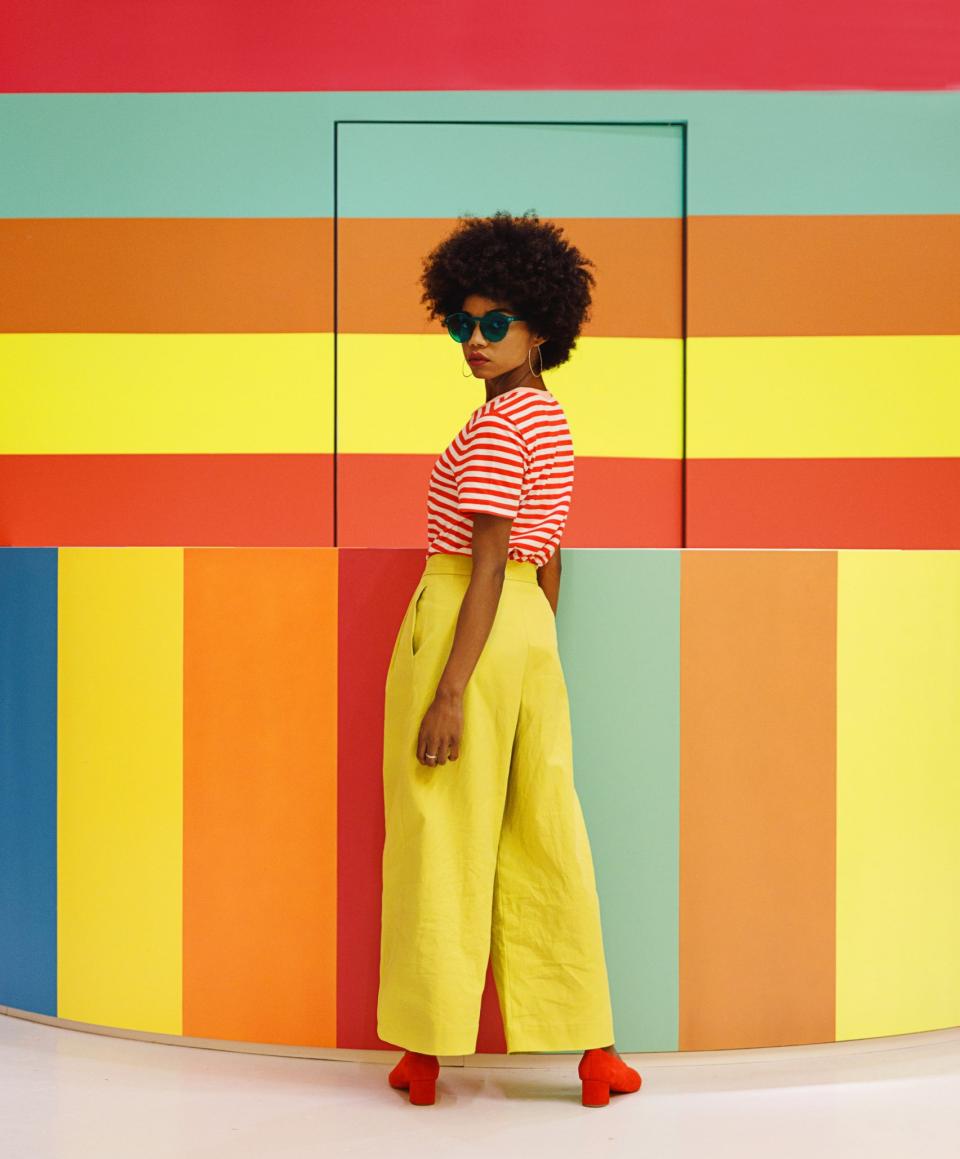 A stylish individual poses in front of vibrant color walls at the Color Factory exhibition in New York City.