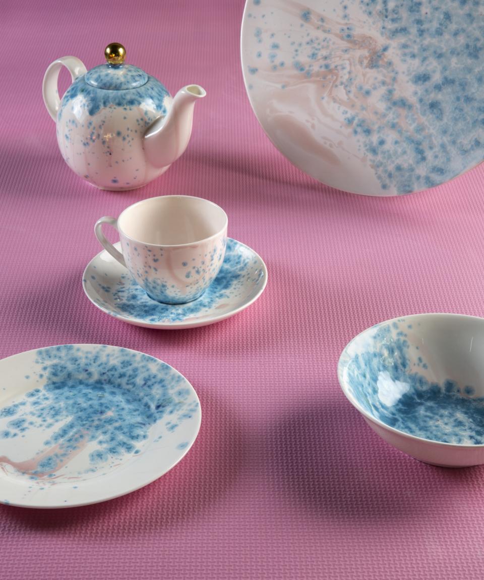 Hand-decorated ceramic and porcelain tableware by Coralla Maiuri featuring a teapot, cup, and saucers with blue designs.