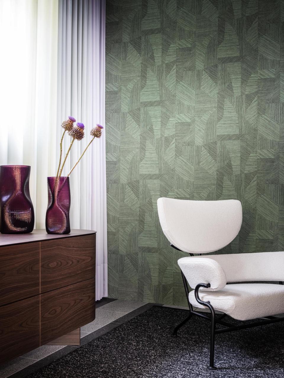 Stylish interior featuring a unique white chair, decorative vases, and textured green wallpaper inspired by the Tangram puzzle.