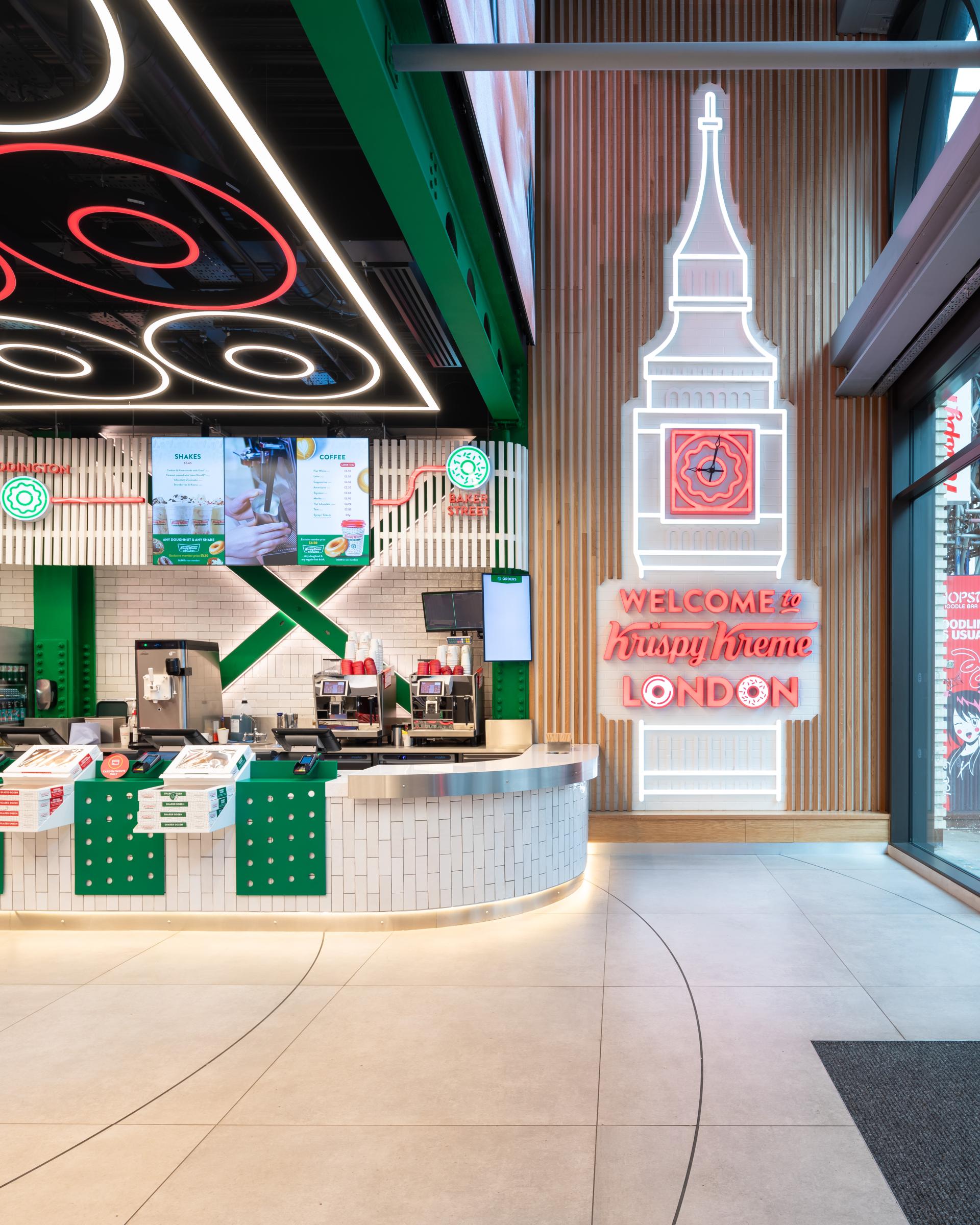 Illuminated counter and neon sign welcome visitors to Krispy Kreme's flagship store in London, showcasing modern design elements.