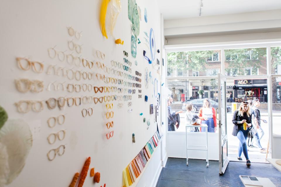 Display of colorful biodegradable eyewear prototypes on a wall, showcasing innovative materials by Crafting Plastics Studio.