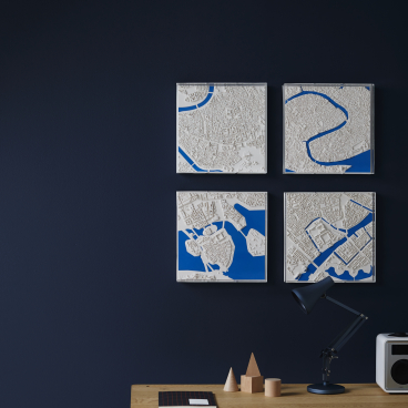 Three-dimensional city maps displayed on a dark wall, showcasing urban landscapes in white and blue tones.