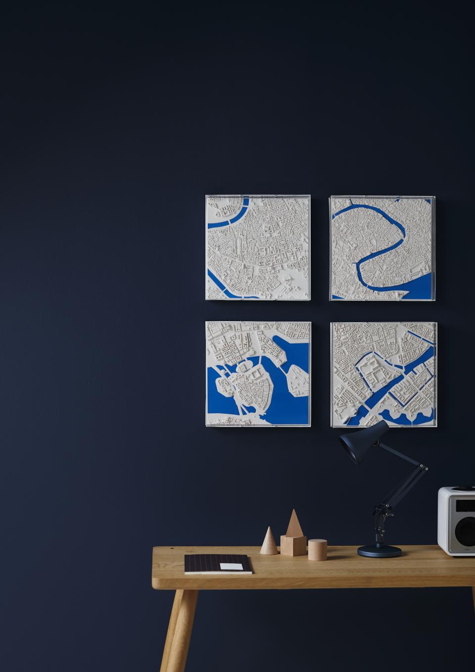 Three-dimensional city maps displayed on a dark wall, showcasing urban landscapes in white and blue tones.