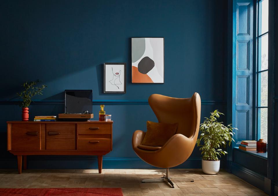 Stylish living room featuring a modern orange chair, wooden furniture, vibrant artwork, and a deep blue wall backdrop.
