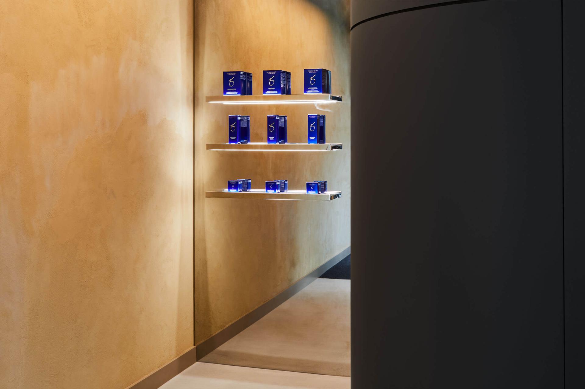 Modern healthcare interior featuring blue product boxes on illuminated shelves against a warm, textured wall at Medika Clinic.