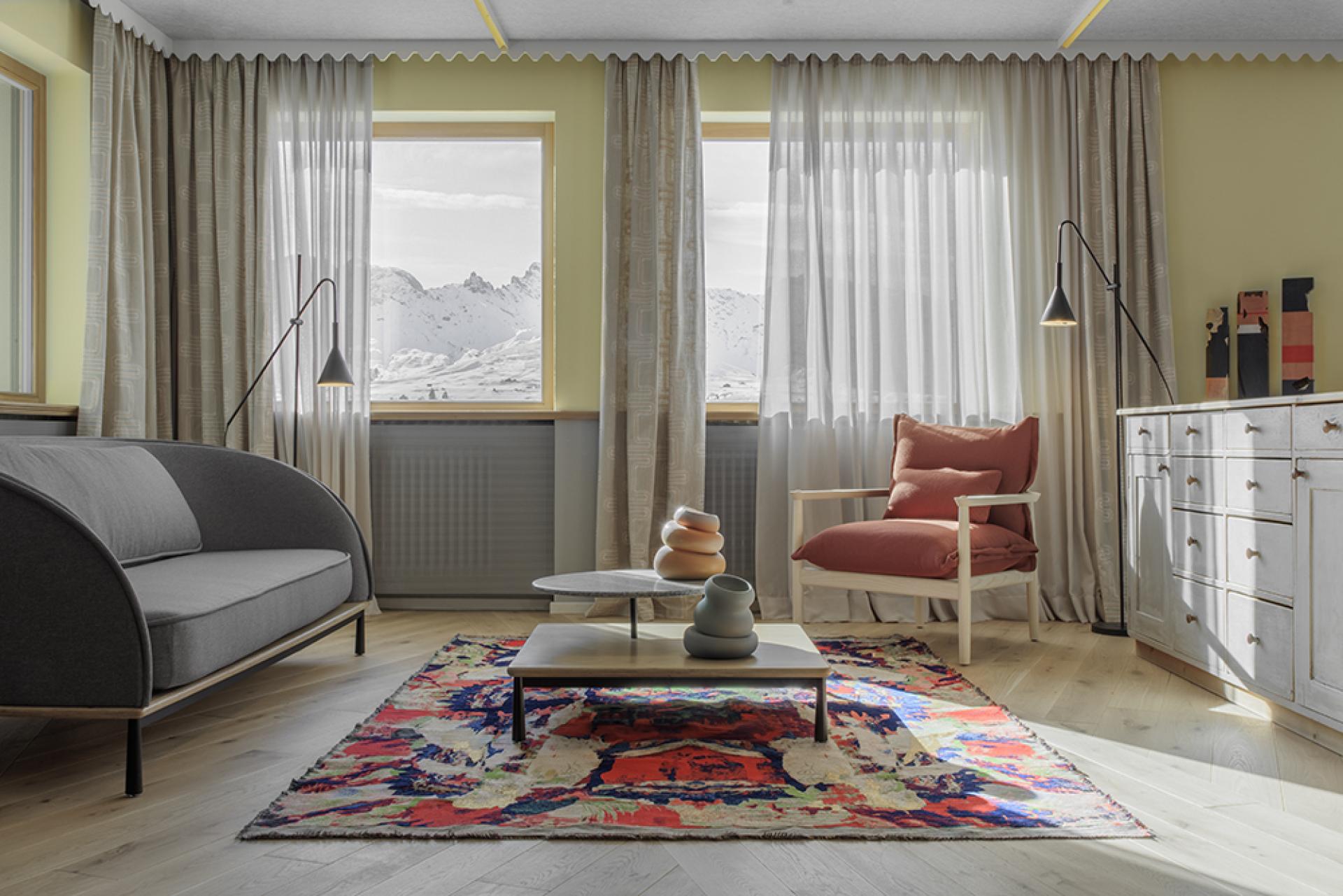 Cozy hotel room featuring modern design, colorful rug, and stunning views of the Dolomite Mountains through large windows.