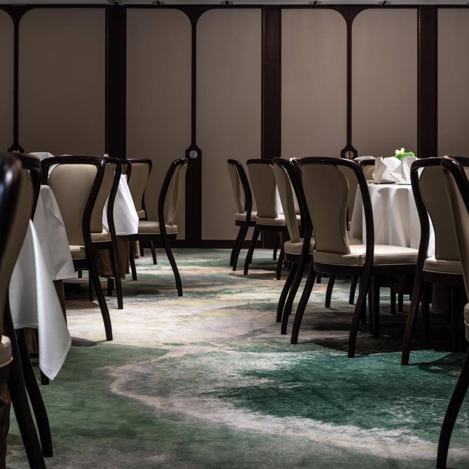 Elegant dining setup in the Canton Room, featuring stylish chairs and a vibrant green carpet, overlooking Victoria Harbour.