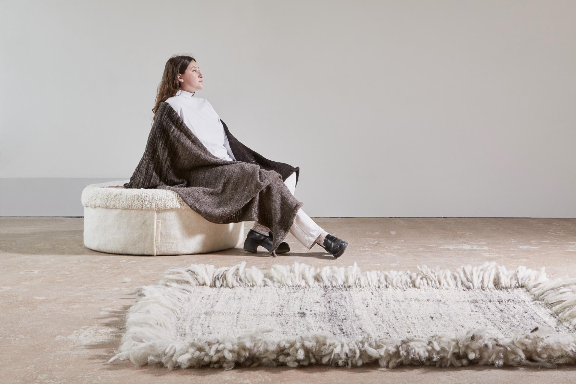 Woman seated on a cozy biomaterial ottoman, surrounded by sustainable textile products and a unique waste-based rug.