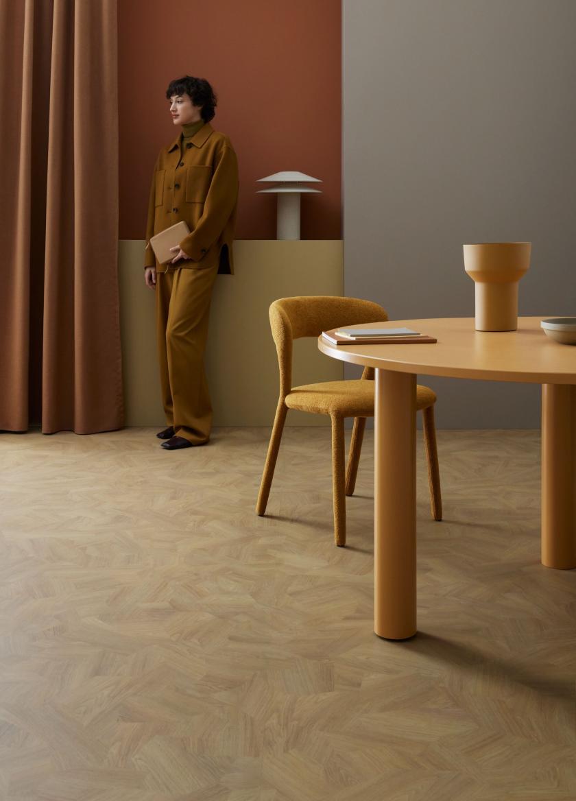 A woman stands against a wall with a table and chairs in the foreground