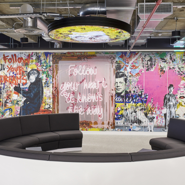 Vibrant office lounge area featuring artistic wall mural and modern circular seating, designed by PENSON for Sports Direct.