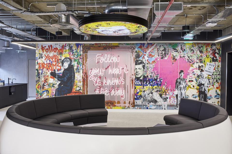 Vibrant office lounge area featuring artistic wall mural and modern circular seating, designed by PENSON for Sports Direct.
