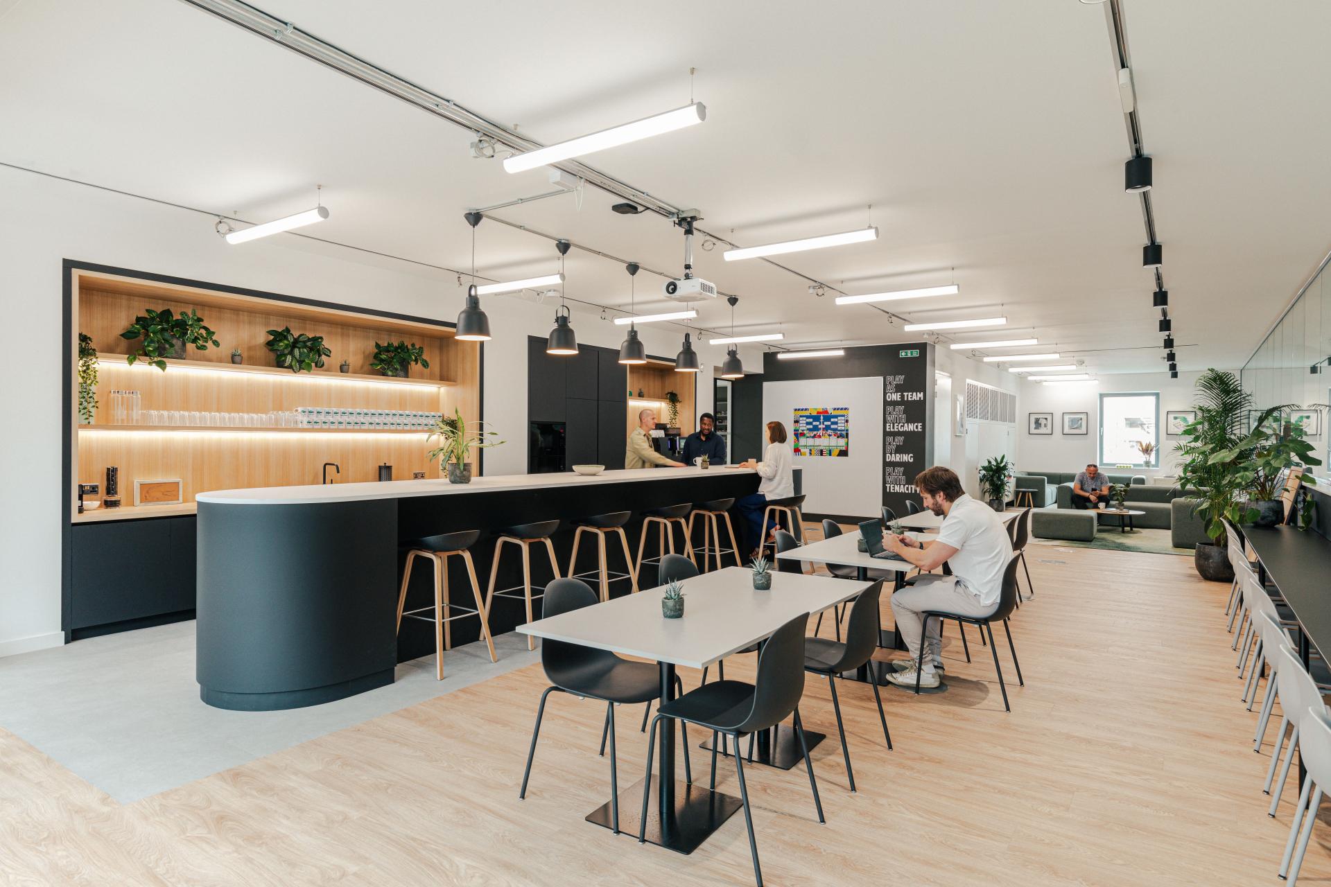 Modern office workspace for Lacoste featuring a stylish bar area, seating arrangements, and green plants in a New York warehouse style.