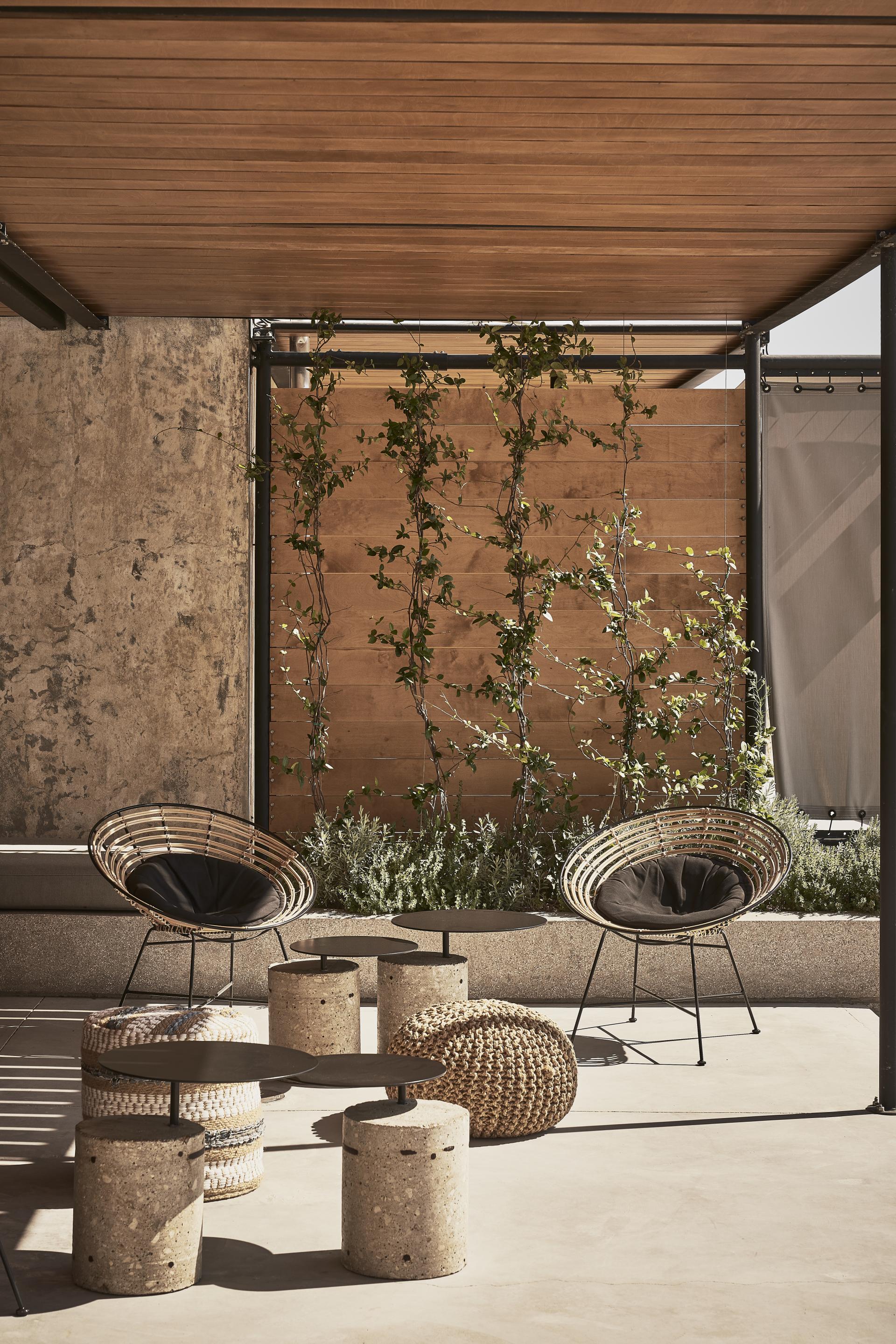 Chic outdoor seating area featuring woven chairs and modern concrete tables amidst greenery, showcasing K-Studio's innovative hotel design.