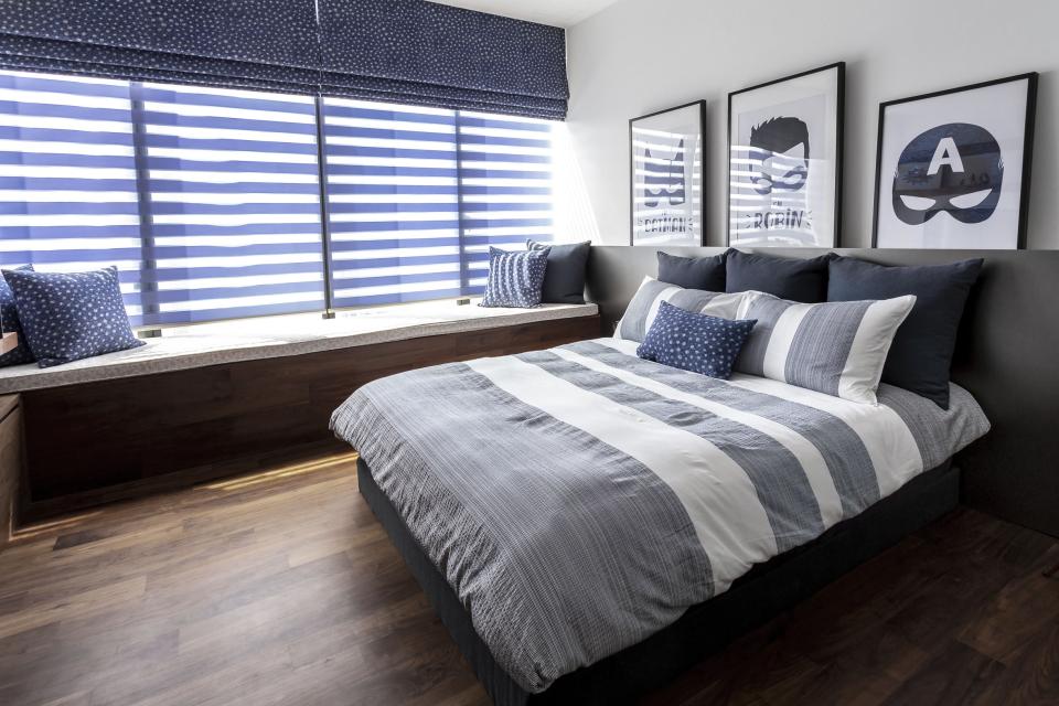 A modern bedroom featuring a striped bedspread, decorative pillows, and artwork, showcasing Elliot James' stylish interior design.