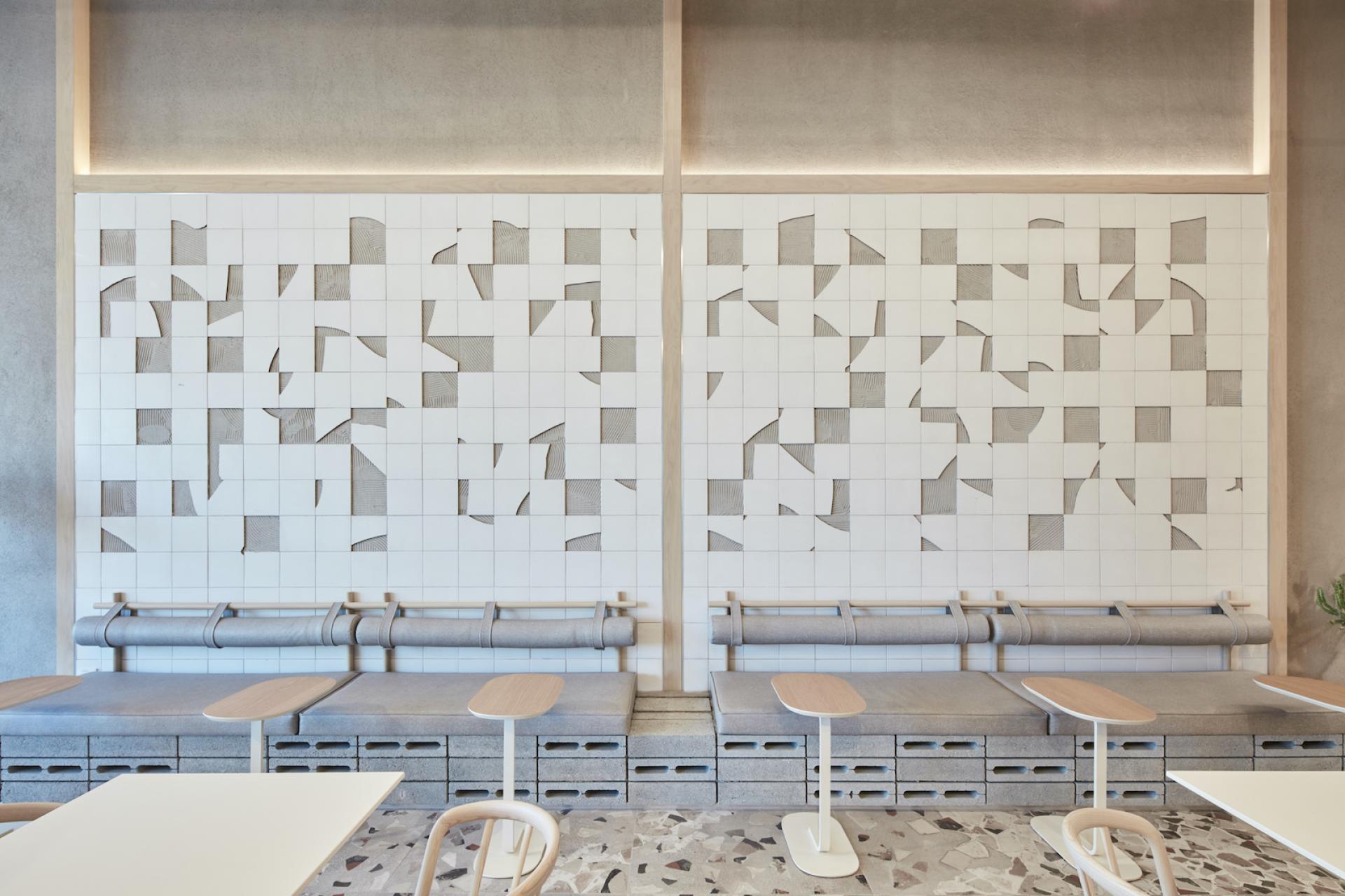 Modern coffee shop interior featuring a textured tiled wall, minimalist furnishings, and raw concrete accents by Roar Studio.