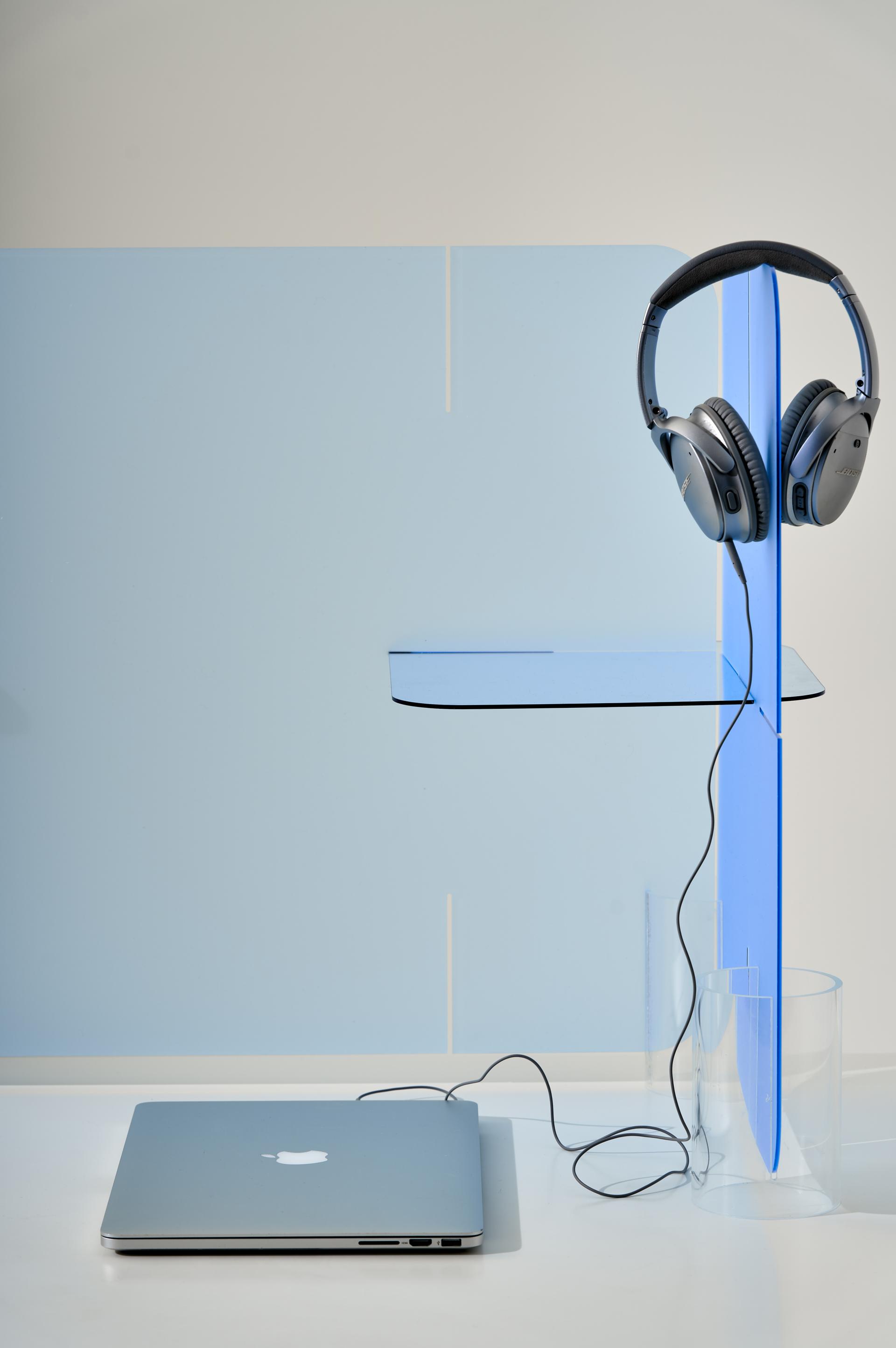 A sleek laptop and headphones are positioned next to a modern blue acrylic partition, symbolizing innovative workspace solutions.