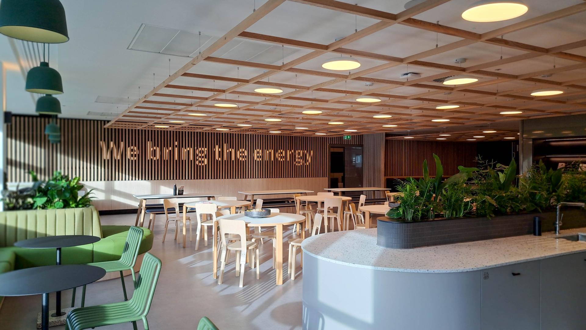 Modern office interior featuring vibrant seating, greenery, and the phrase "We bring the energy" prominently displayed.