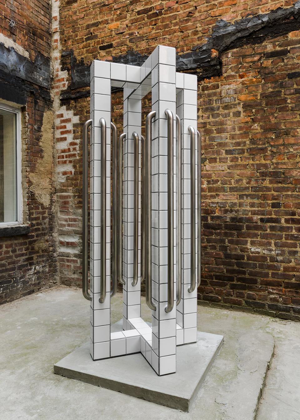 Sculptural installation by Zac Hacmon, featuring subway tiles and metal handles against a brick wall background.