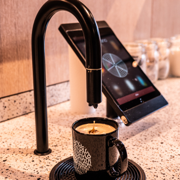Premium coffee pouring into a stylish black mug beside a touchscreen coffee machine at Colony workspace.