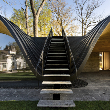 Fold House features a striking curved staircase leading to a contemporary structure, seamlessly blending architecture with nature in Southern Ontario.