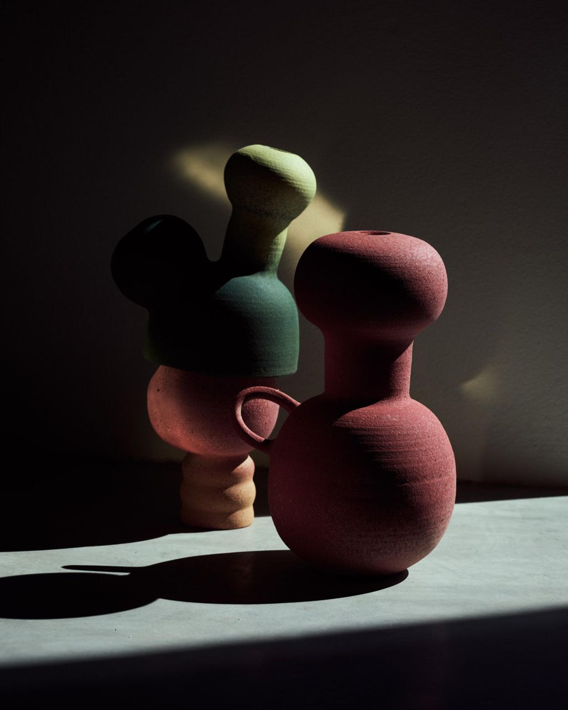 Colorful, sculptural ceramic vases by Sandra Berghianu casting shadows on a surface, showcasing unique design and craftsmanship.