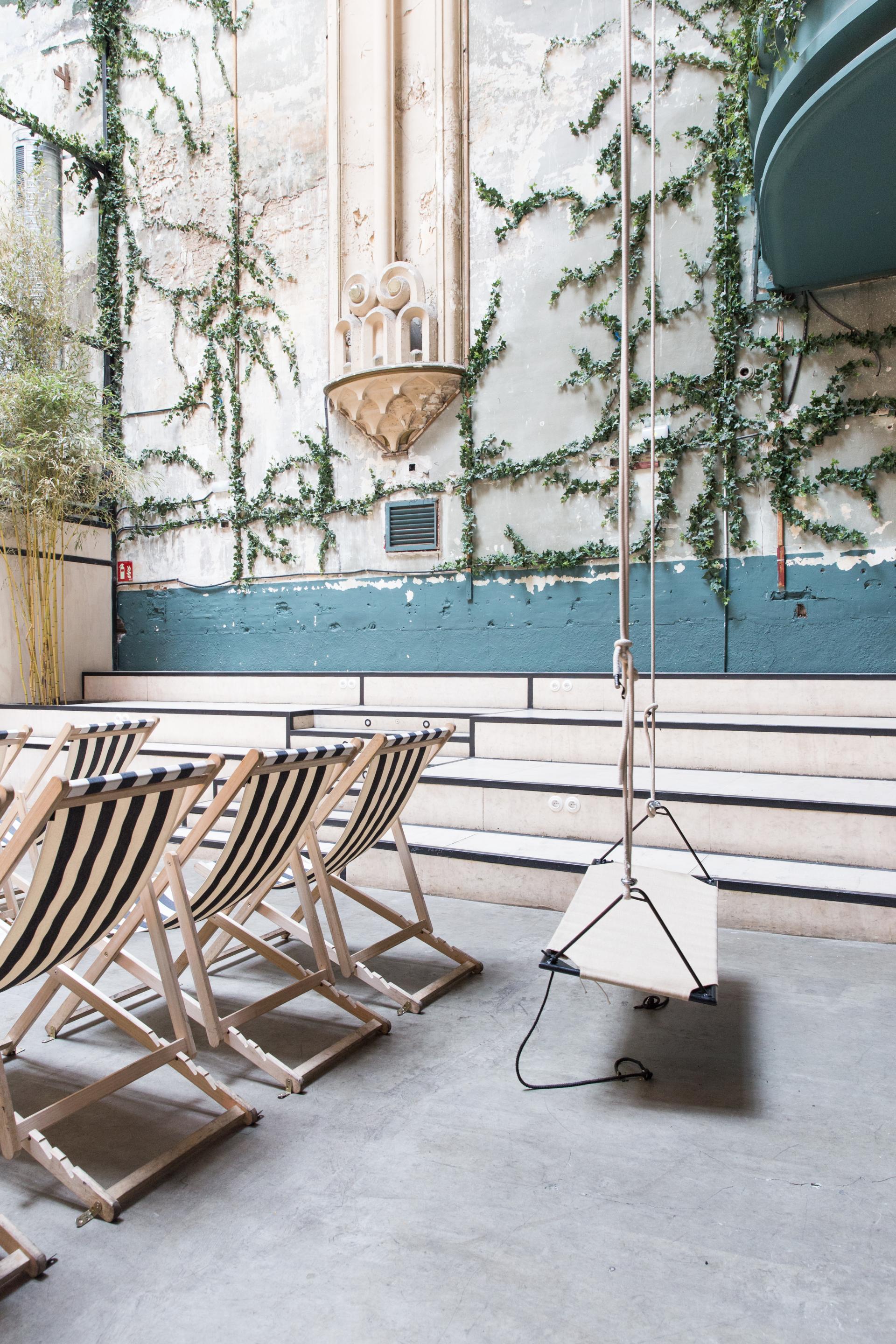 Stylish striped deck chairs face a vintage wall adorned with ivy, enhancing the ambiance of the renovated erotic cinema.
