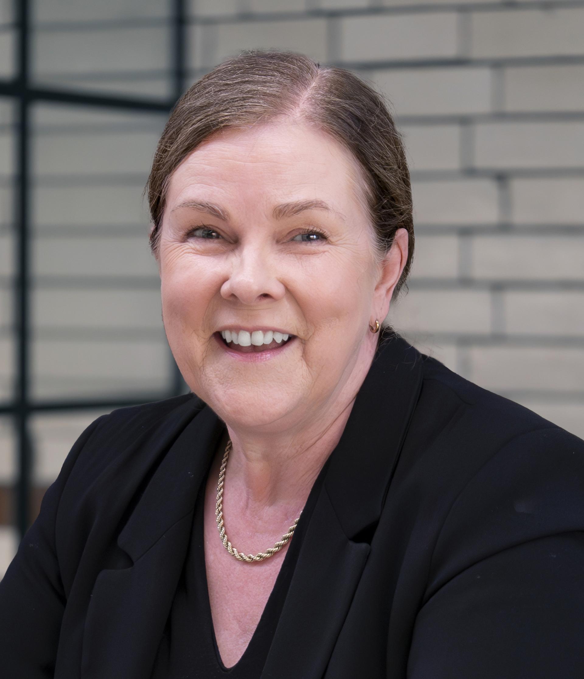 Professional woman smiling in a black blazer, representing Manchester's property discussion and residential mix.