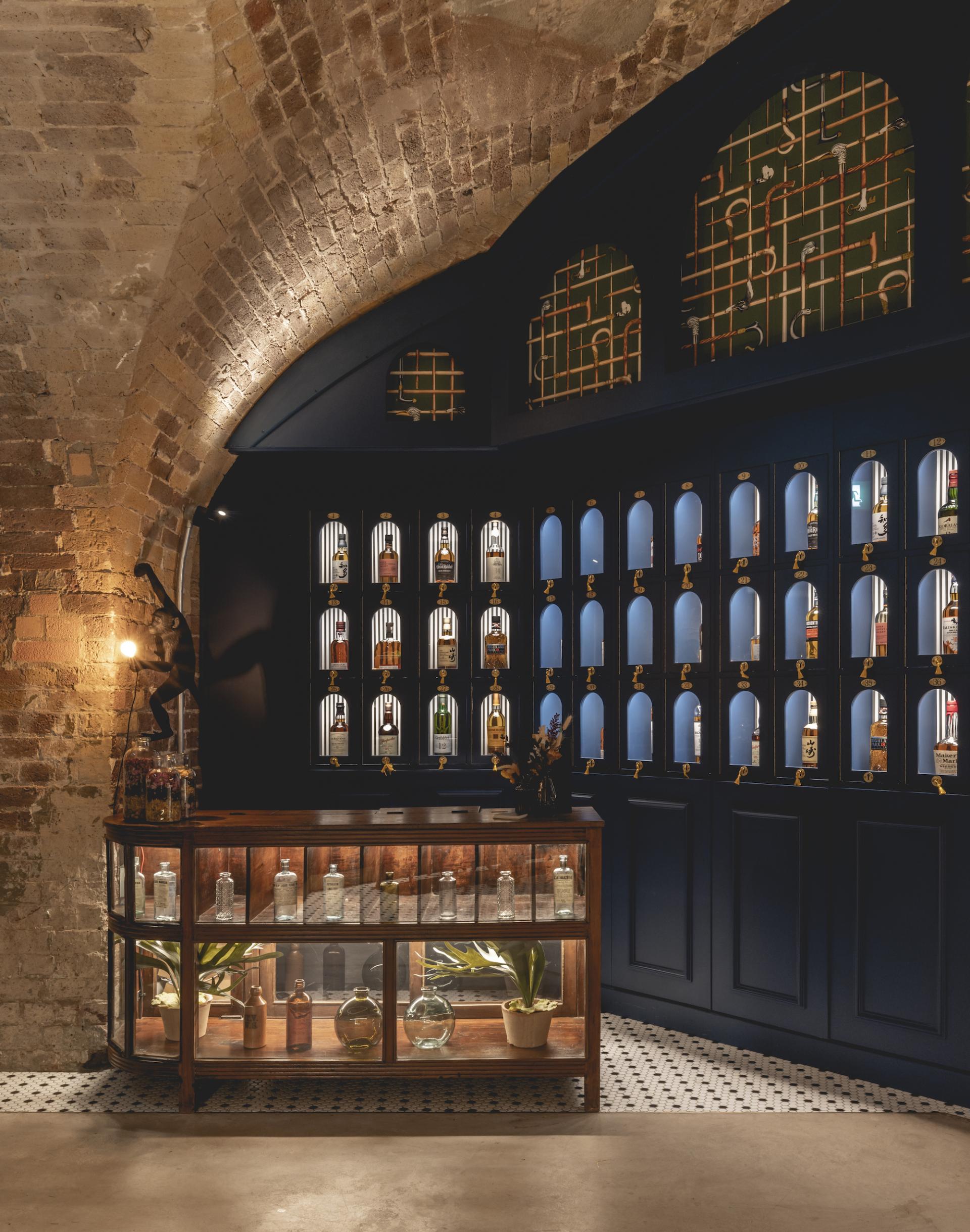 Stylish bar area featuring a wooden display cabinet, glass bottles, and elegant decor at The Libertine in the Royal Exchange.