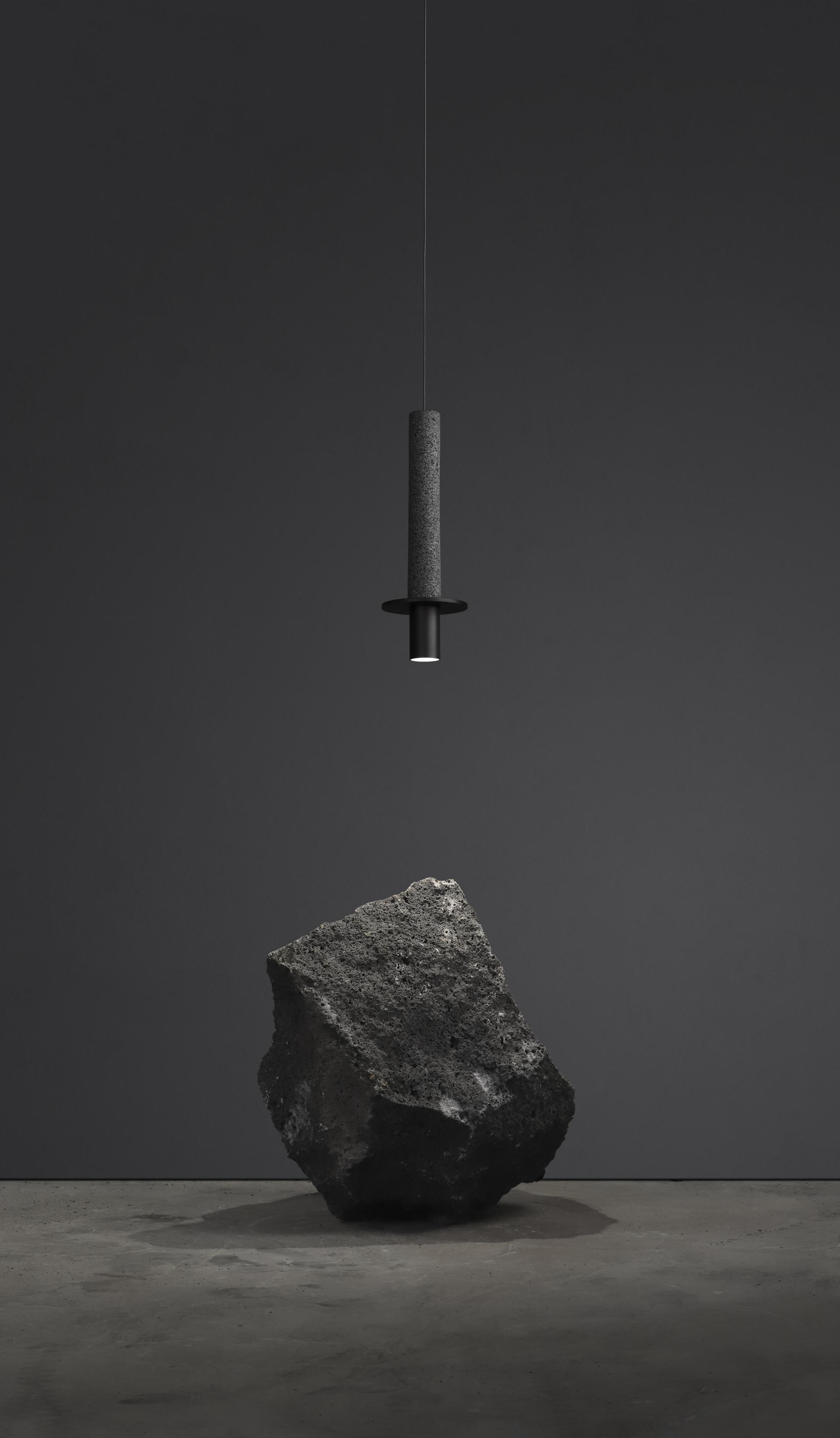 Hanging pendant light featuring a sleek design above a textured rock on a smooth concrete surface.