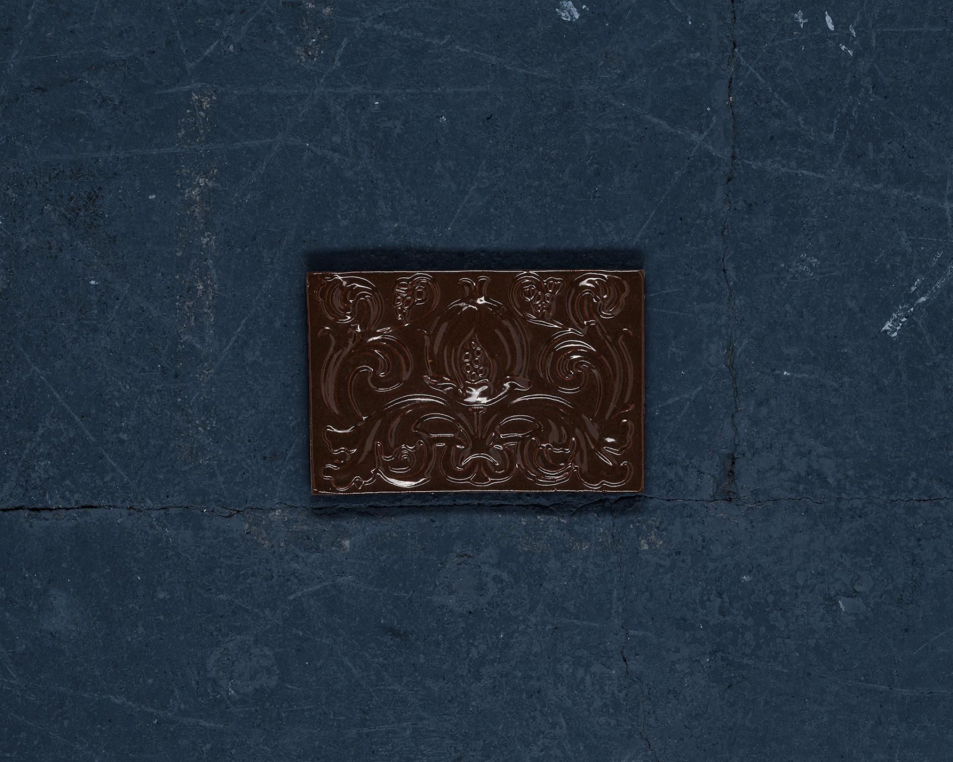 Decorative brown tile created from recycled waste, showcased on a textured dark surface, promoting sustainability in design.