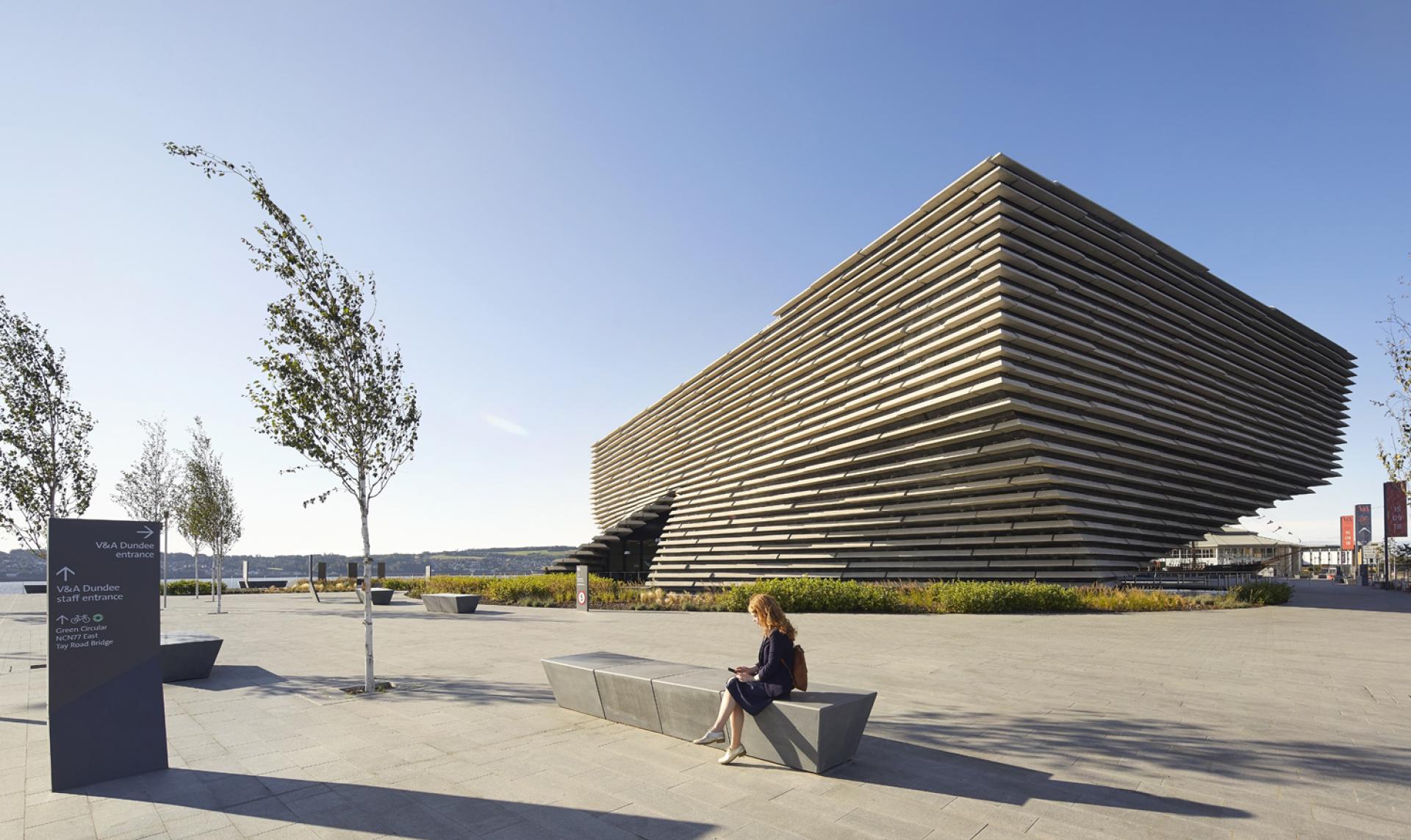 V&A Dundee's striking exterior features Kengo Kuma's innovative design, set against a clear blue sky with landscaped surroundings.