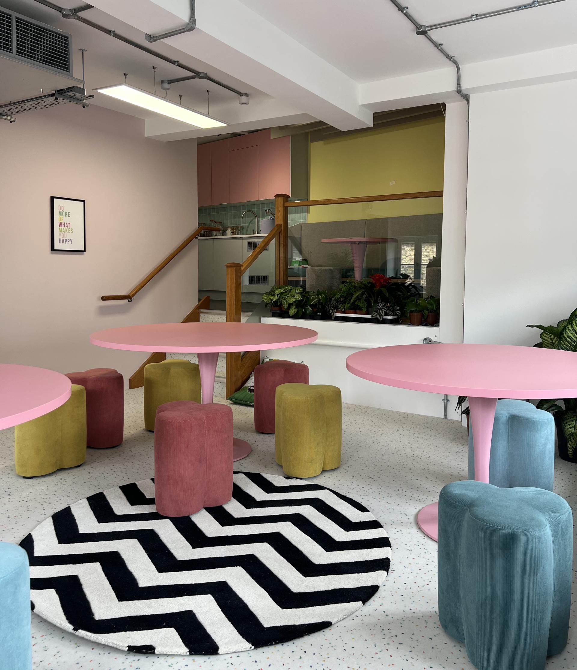 Brightly colored tables and stools in a lively workspace, complemented by a stylish rug and greenery.