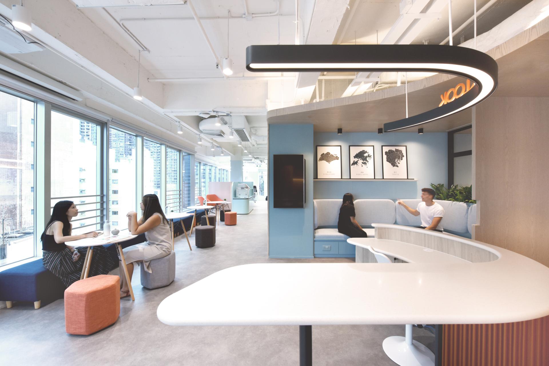 Modern office interior design featuring collaborative workspaces, comfortable seating, and large windows showcasing a city view.