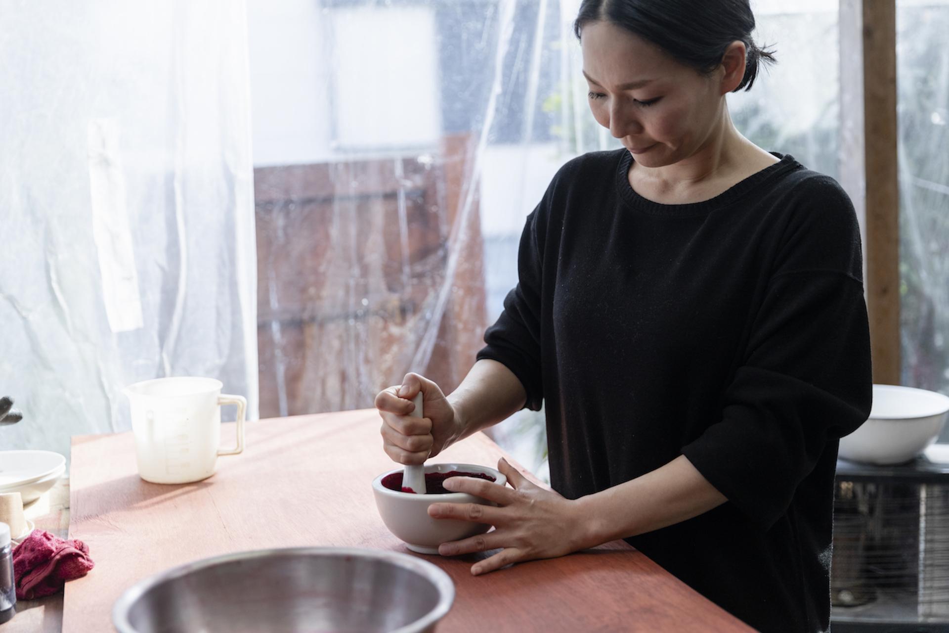 A woman skillfully prepares natural dye in a bowl, showcasing traditional Japanese dyeing techniques at Japan House London.