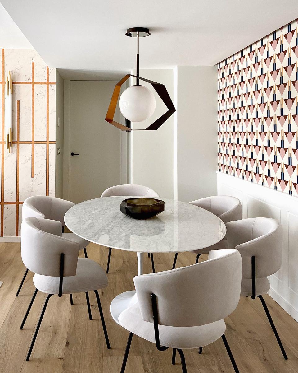Modern dining area featuring a distinctive black and gold pendant light over a round marble table with plush cream chairs.