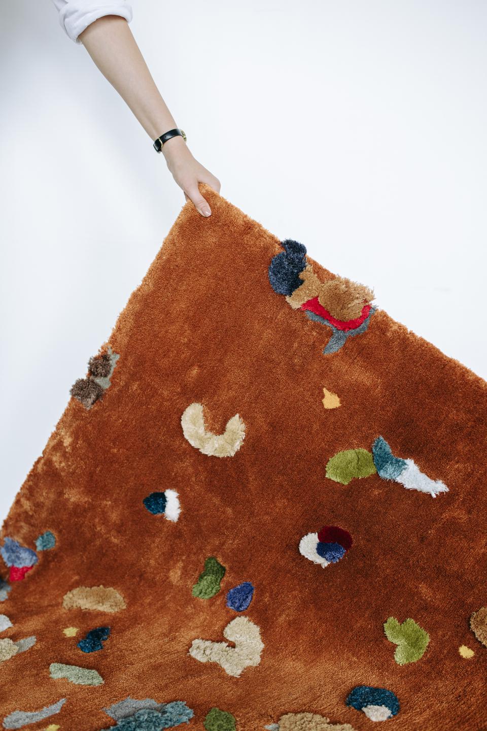 Soft, colorful Chaos Rug designed by Audronė Drungilaitė, showcasing abstract patterns in vibrant hues on a warm brown background.